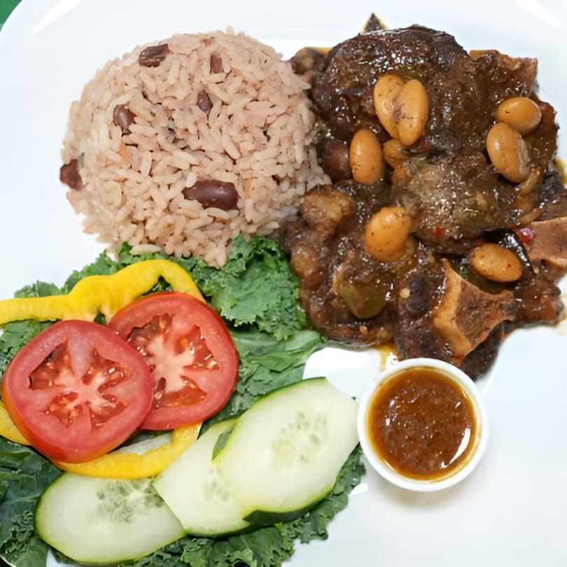 Jamrock Grill's Caribbean oxtail stew with rice and peas, fresh salad, and a side of sauce.