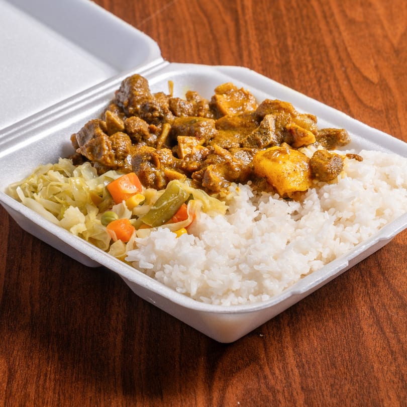 Jamrock Grill's curry goat with white rice and steamed vegetables in a takeout container.