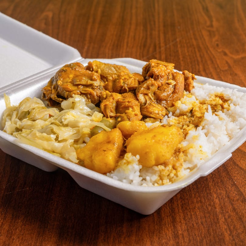 A Jamrock Grill Caribbean curry chicken meal with rice, cabbage, and potatoes in a takeout container.